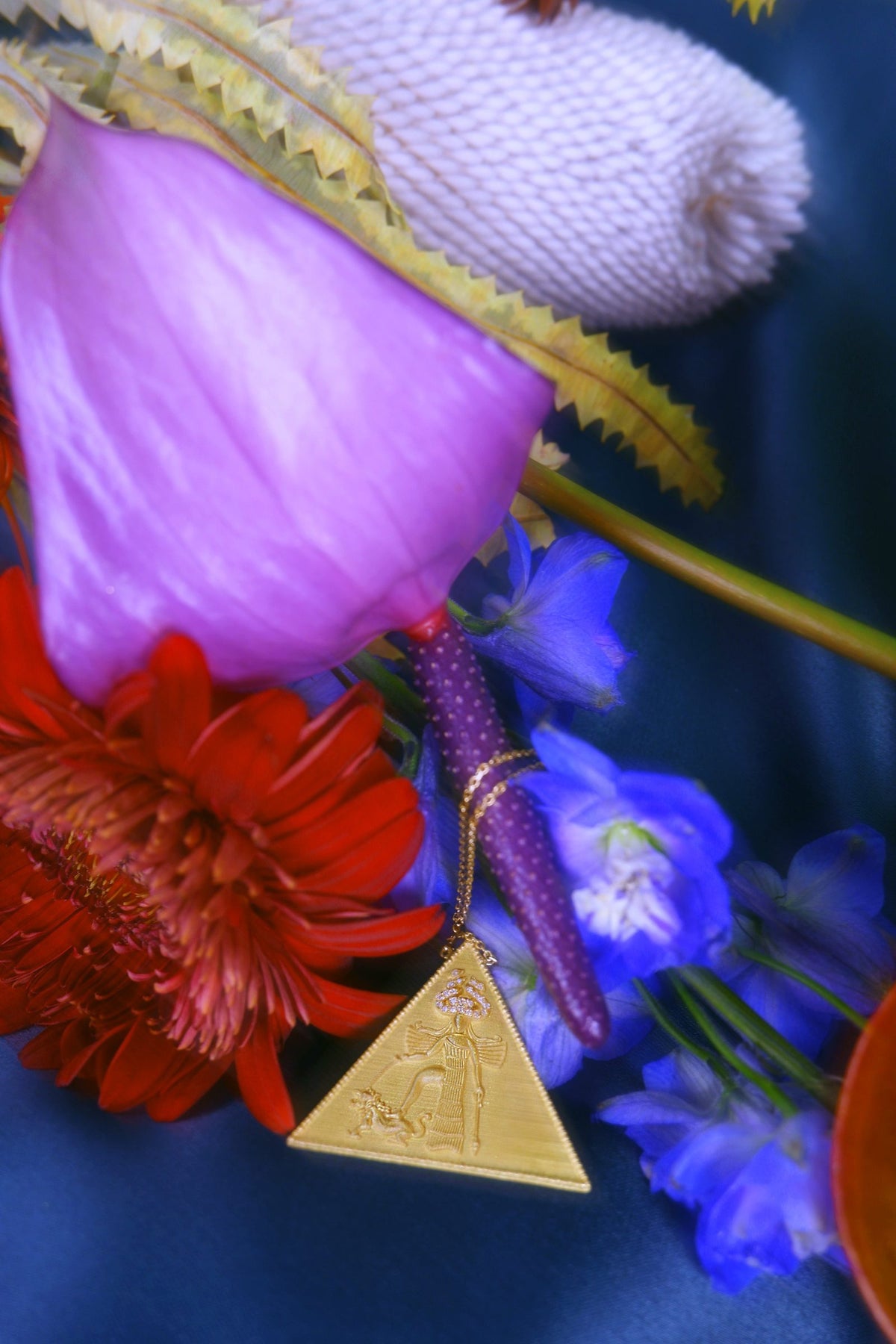 Ishtar Necklace in 18K yellow gold resting among purple and red flowers